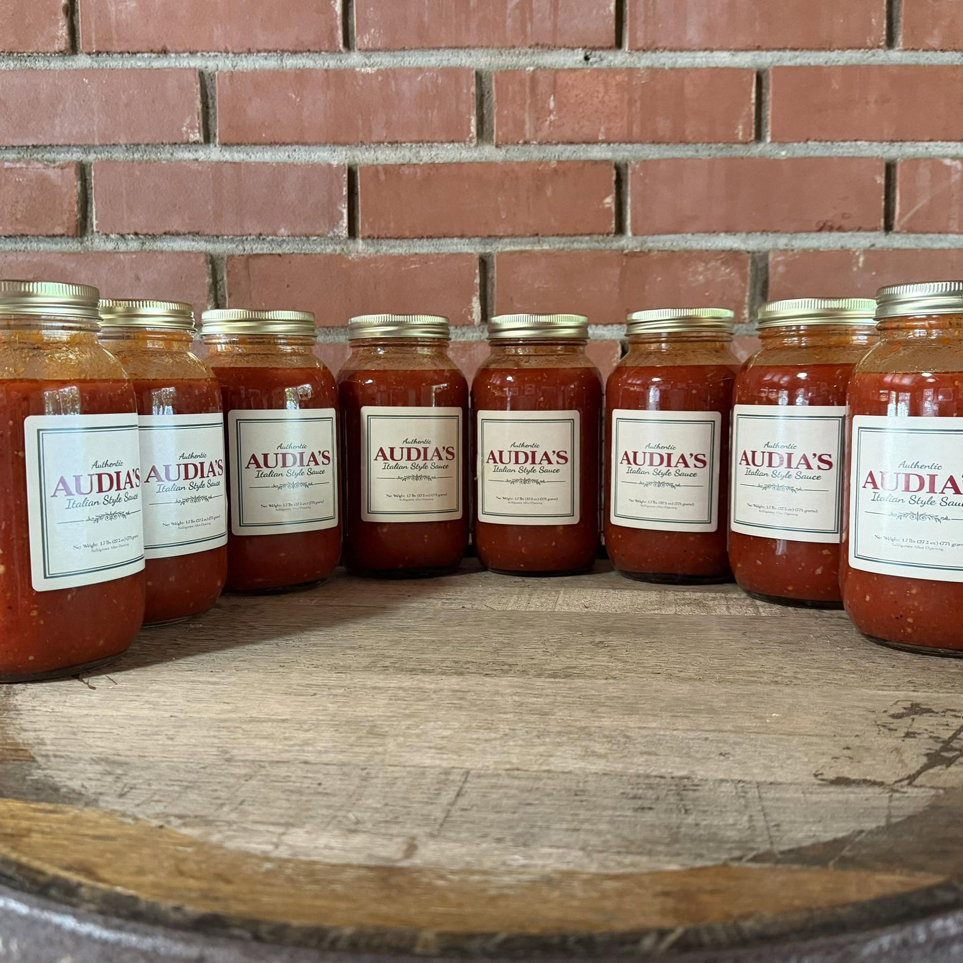 A row of Audia's Italian style sauce jars on a wooden barrel